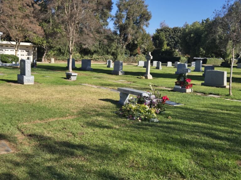 Block N - Monument Lot with gravestones, green grass, trees, and floral arrangements.