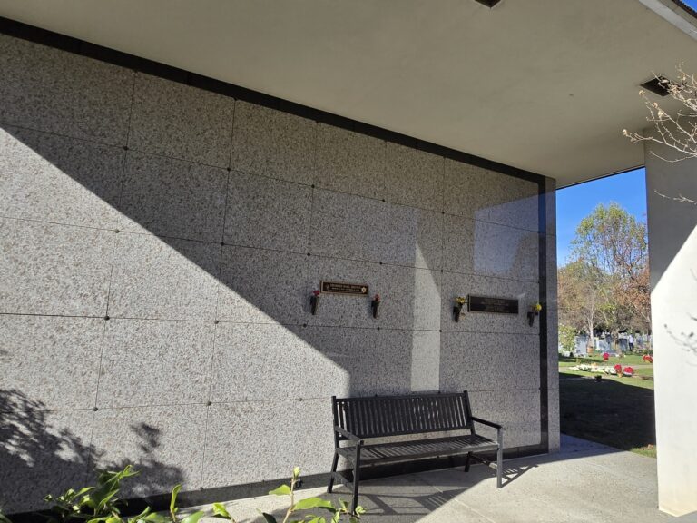 Heritage Mausoleum - True Companion Crypt with a stone wall, crypt slots, and a black bench in a shaded area.