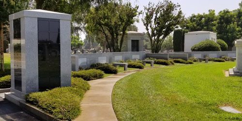 Vista Columbarium Companion Niche with a stone structure, curved pathway, grass, and surrounding trees.